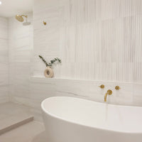 Modern bathroom with a freestanding bathtub, gold fixtures, and decorative elements.