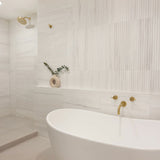 Modern bathroom with a freestanding bathtub, gold fixtures, and decorative elements.