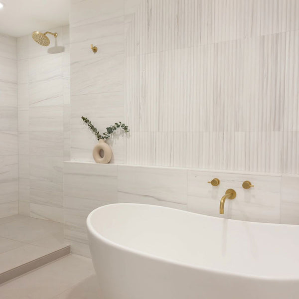 Modern bathroom with a freestanding bathtub, gold fixtures, and decorative elements.
